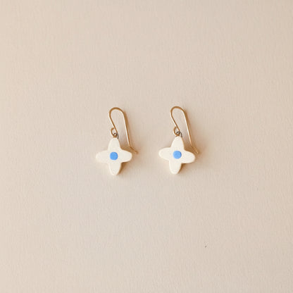 four petal-shaped  flower earrings with blue centers on warm sand colored background