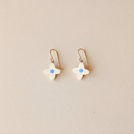 four petal-shaped  flower earrings with blue centers on warm sand colored background